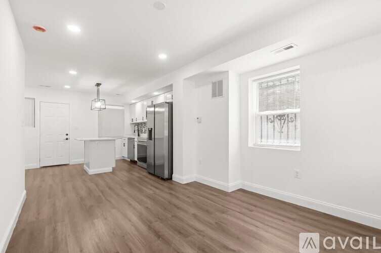 A spacious room with wooden flooring and a kitchen area with white appliances.