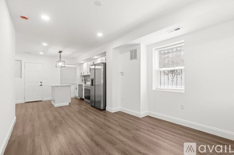 A spacious room with wooden flooring and a kitchen area with white appliances.