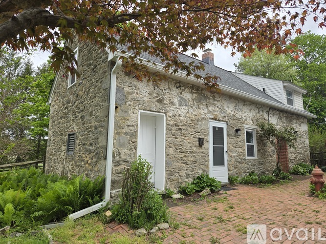 A small stone house with a white door and windows surrounded by greenery.