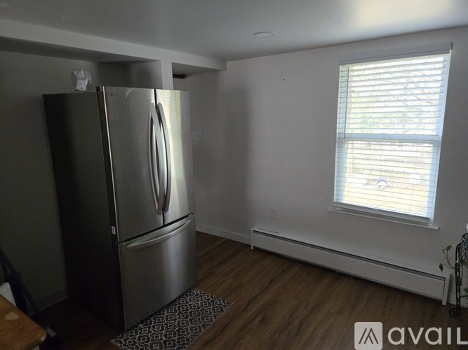 A stainless steel refrigerator in a room with wooden flooring and a window with blinds.