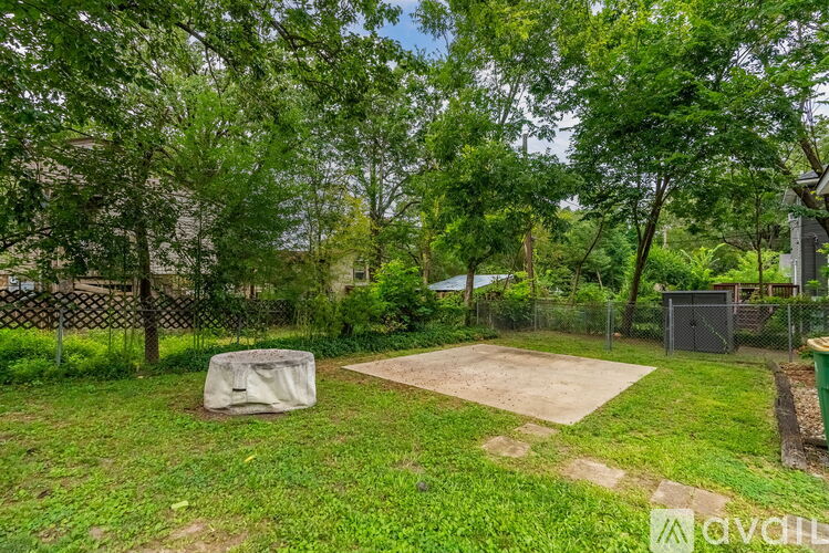 A backyard with a fence, trees, and a covered grill area.