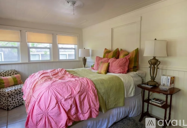 A bedroom with a bed covered in a pink comforter and a green throw.