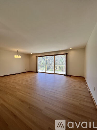 A spacious room with wooden flooring and large windows.