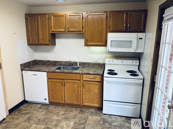 A kitchen with a white dishwasher, white stove, and wooden cabinets.