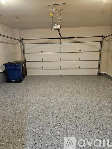 A room with a grey floor and a blue bin.