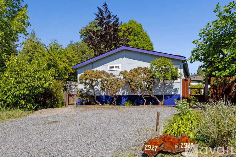 A gravel driveway leads to a white building with a blue roof.