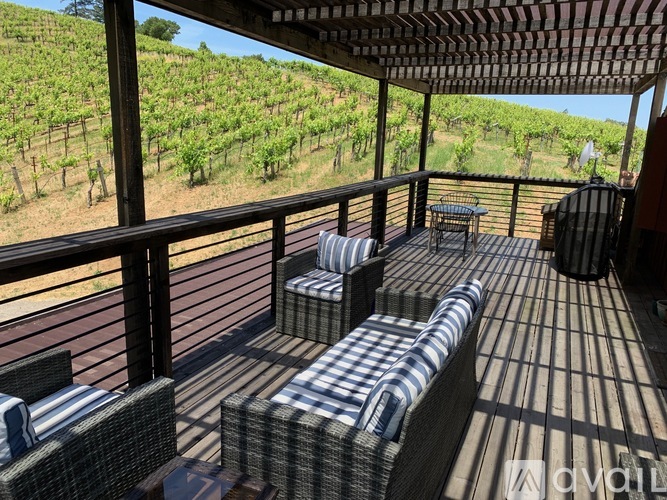 A wooden deck with a table and chairs overlooking a vineyard.