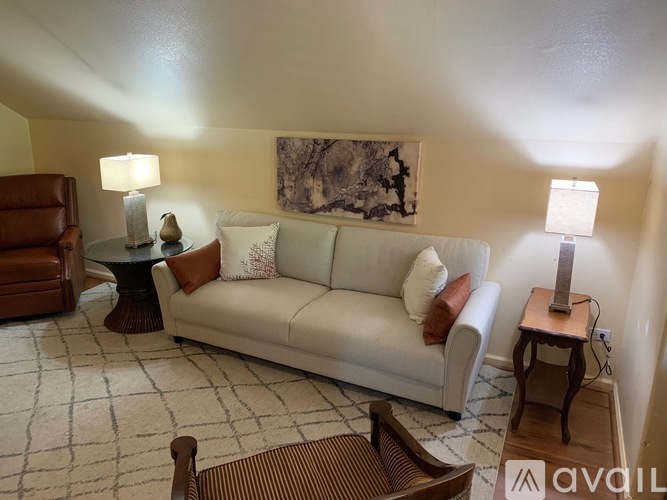 A living room with a couch, two chairs, and a table with a lamp on it.