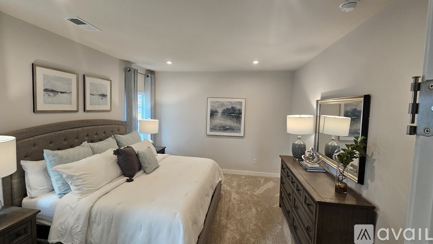 A bedroom with a large bed, a nightstand with a lamp, and two framed pictures on the wall.