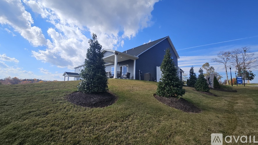 A house with a blue roof and white walls is surrounded by a grassy lawn and trees.