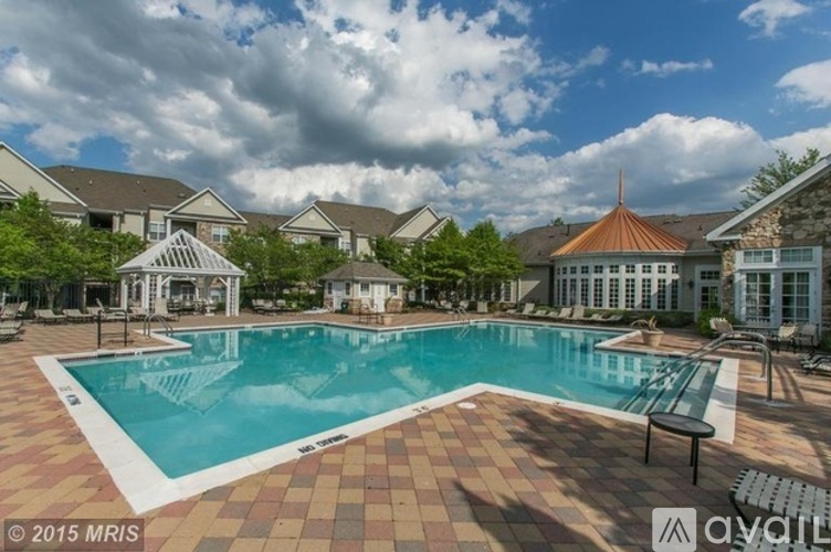 A large swimming pool surrounded by a brick patio and lounge chairs.