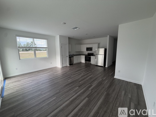 A spacious living room with wood flooring and a kitchen in the background.