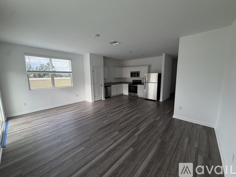 A spacious living room with wood flooring and a kitchen in the background.