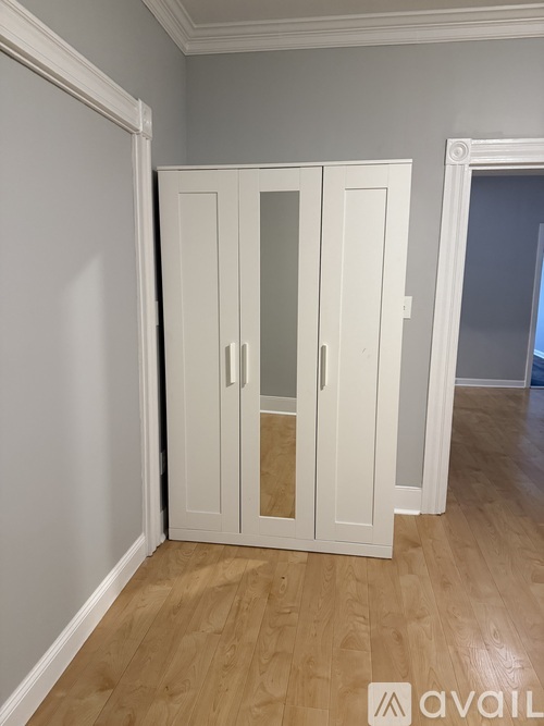 A white double wardrobe with glass doors stands in a room with wooden flooring.