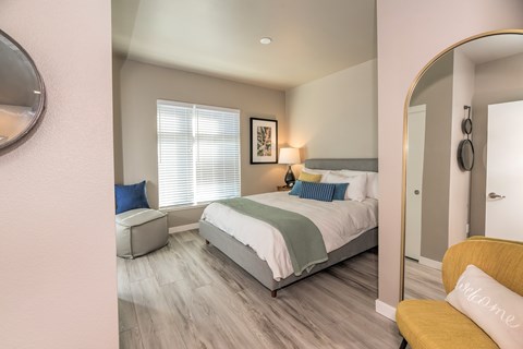 A bedroom with a bed, a yellow chair, and a mirror on the wall.
