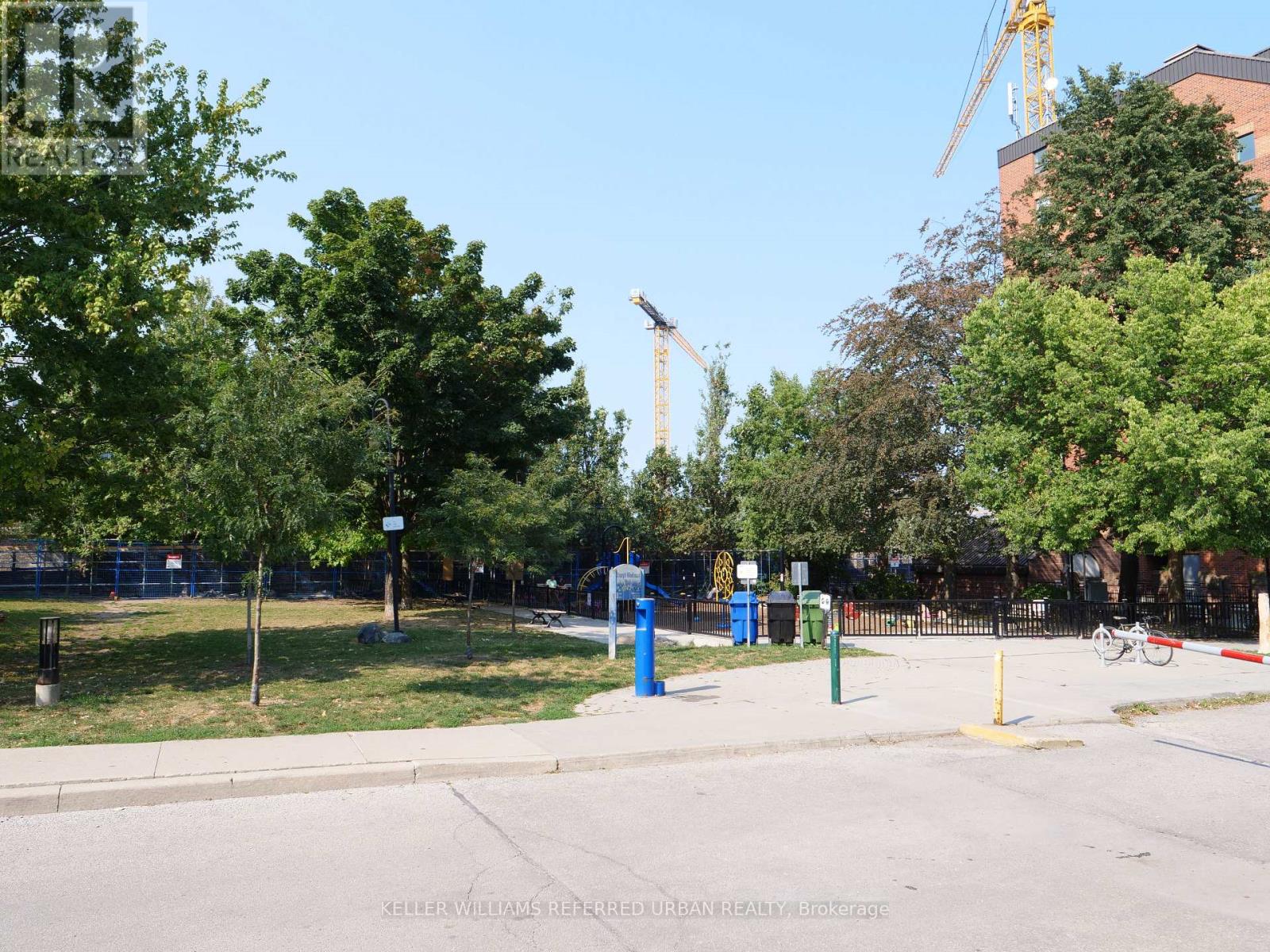 A construction crane is visible in the background of a park with trees and a blue trash can.