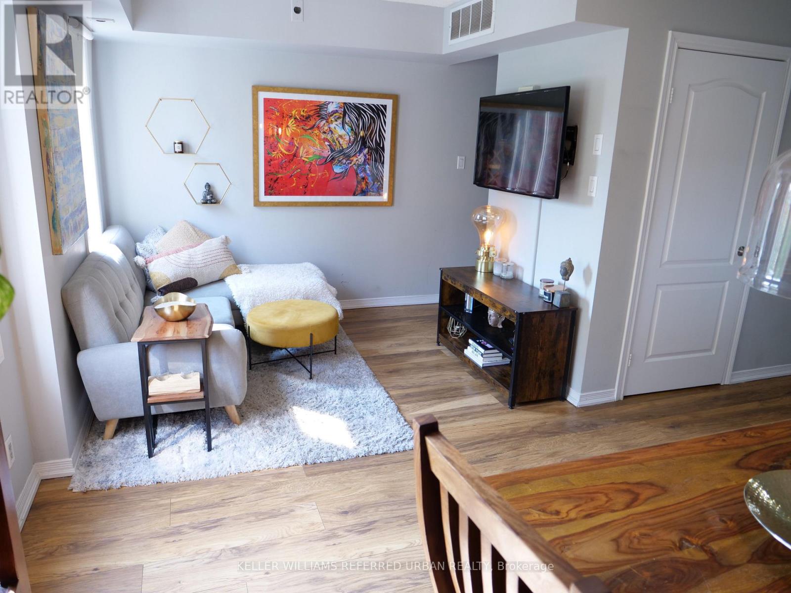 A living room with a grey couch, a yellow ottoman, a wooden coffee table, a TV, and a painting on the wall.