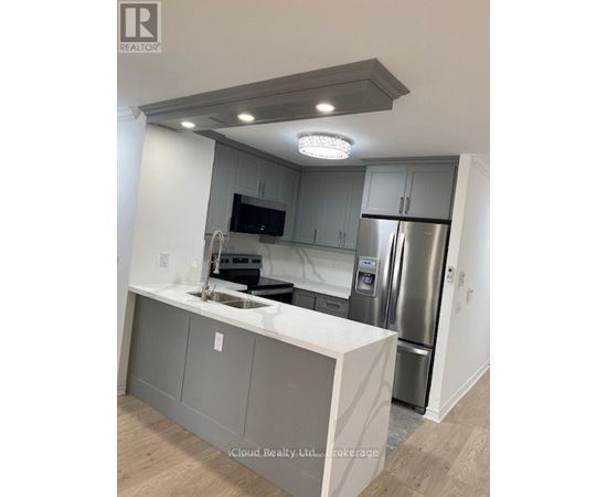 A modern kitchen with a stainless steel refrigerator and a flat screen TV mounted above the sink.