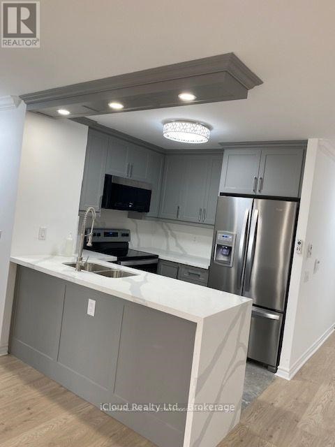 A modern kitchen with a stainless steel refrigerator and a flat screen TV mounted above the sink.