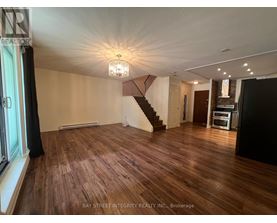 A spacious room with wooden flooring and a staircase in the background.
