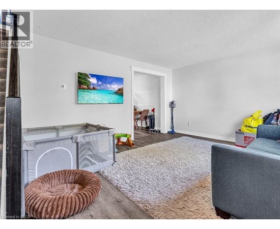 A living room with a grey couch, a white rug, and a painting of a beach scene on the wall.