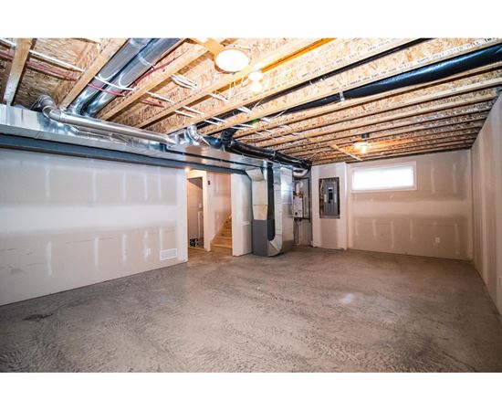 A spacious unfinished basement with concrete floors and exposed ceiling beams.