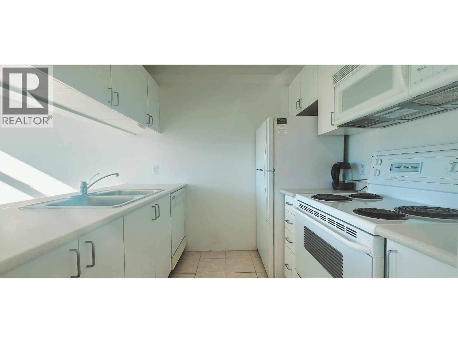 A white kitchen with a sink, stove, and cabinets.