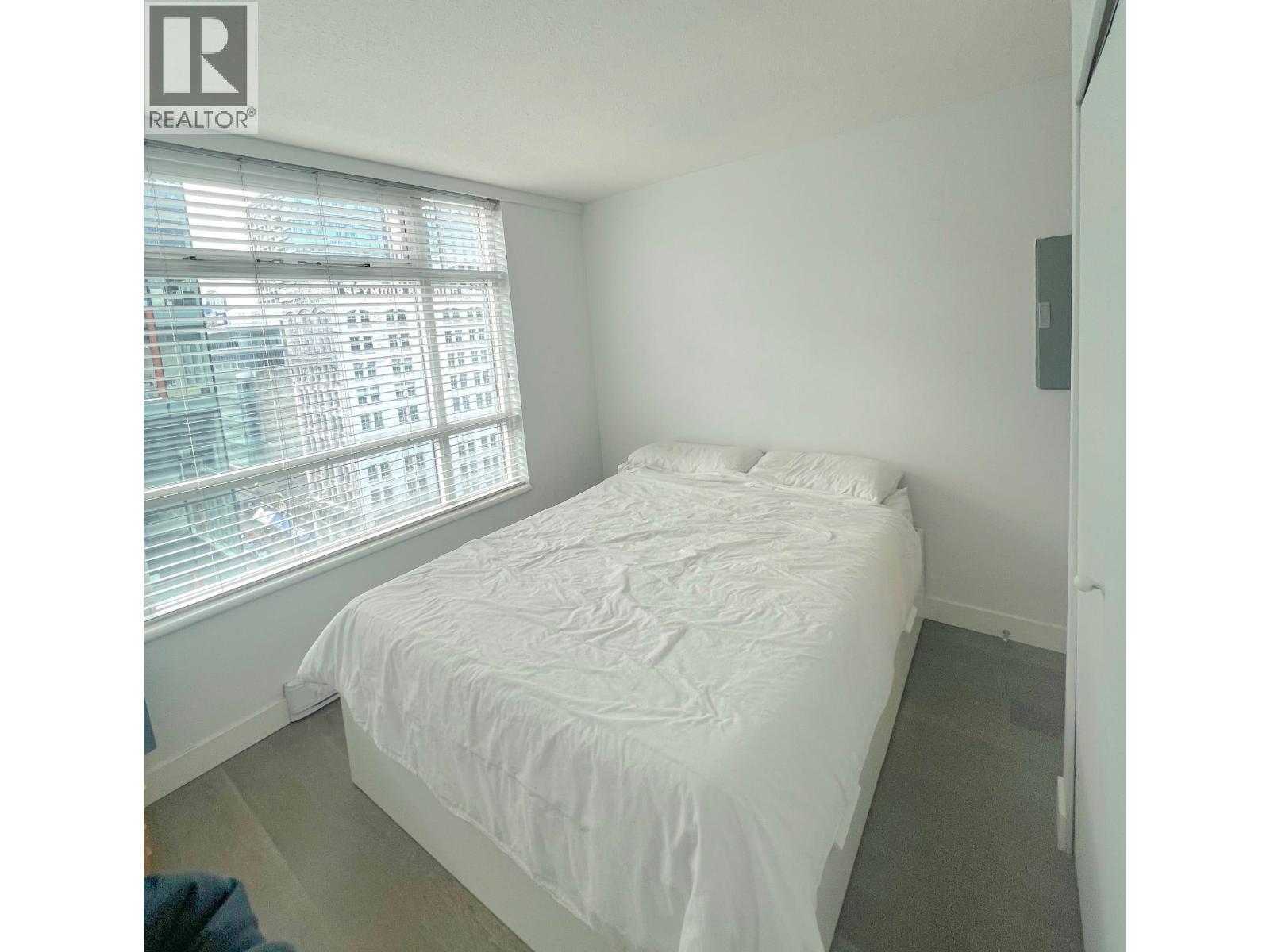 A bedroom with a large bed and a window overlooking a cityscape.