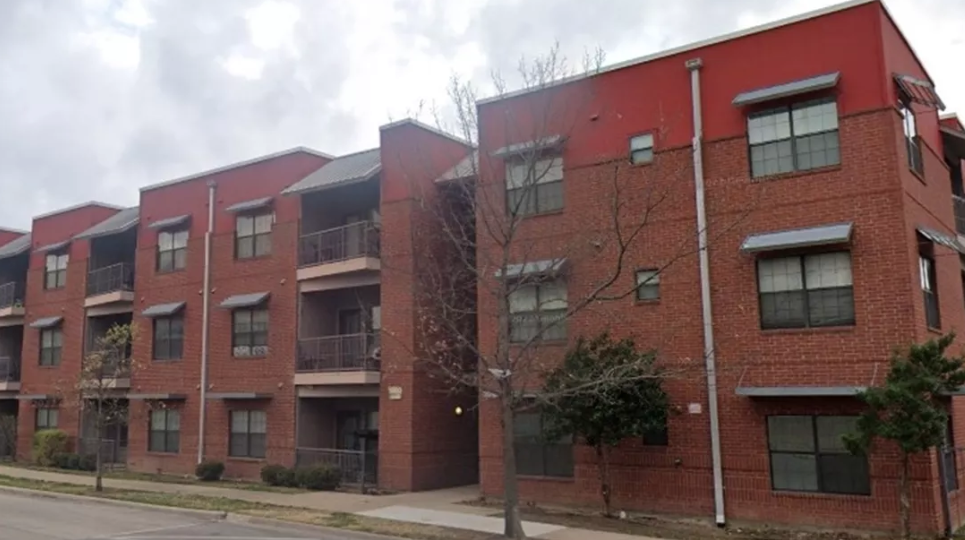 A red brick apartment building with a tree in front.
