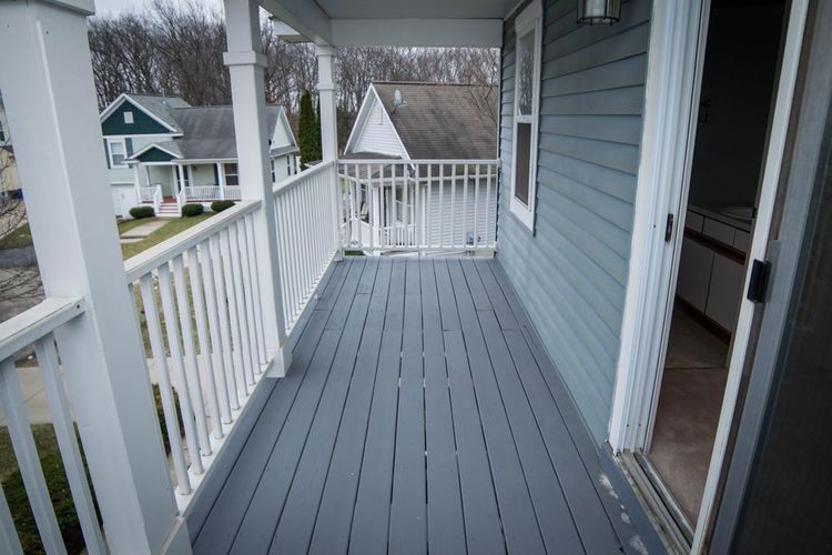 A porch with a white railing and a grey floor.