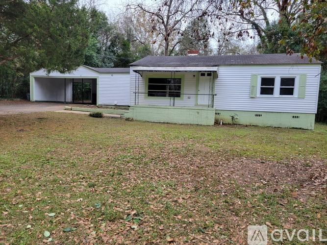 A white house with a green door and windows is surrounded by trees.
