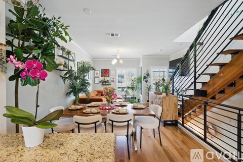 A living room with a dining table and chairs, a staircase, and a plant.
