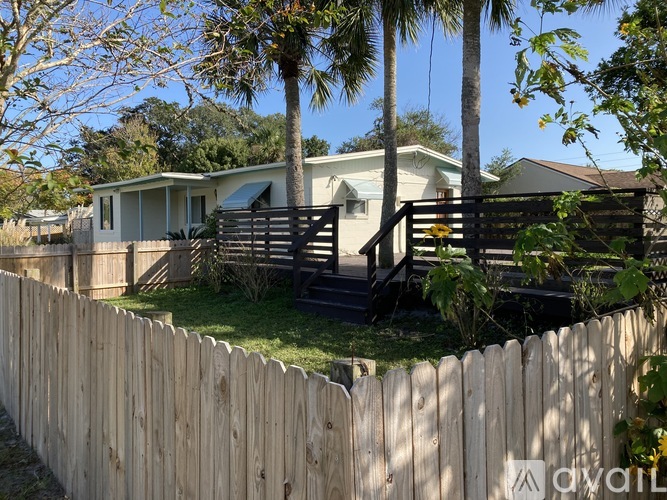 A house with a wooden fence and a palm tree in front.