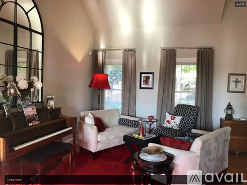 A living room with a piano, two couches, and a table with a vase of flowers on it.
