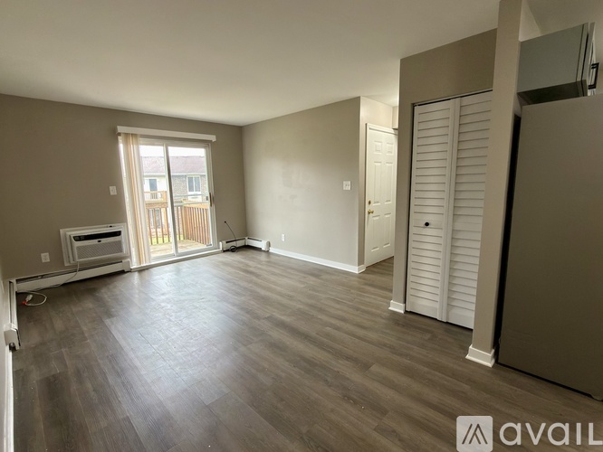 A spacious room with wooden flooring and a sliding glass door leading to a balcony.