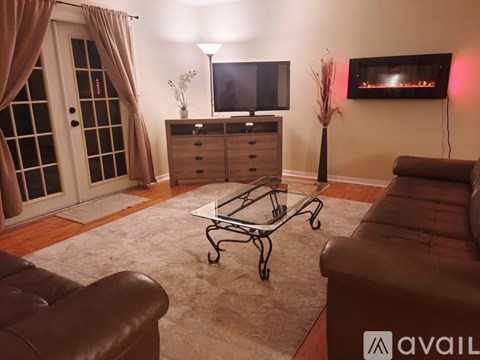 A living room with a brown leather couch, a glass coffee table, and a television on a cabinet.