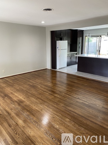 A room with wooden flooring and a kitchen area in the background.