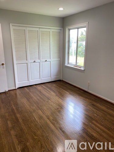 A room with wooden floors and white walls, with a window and a set of white closet doors.