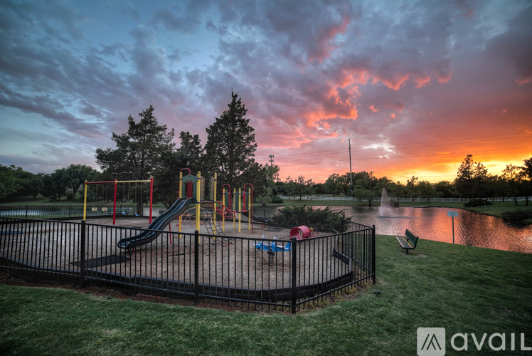 A playground with a slide and swings is surrounded by a fence and a pond.