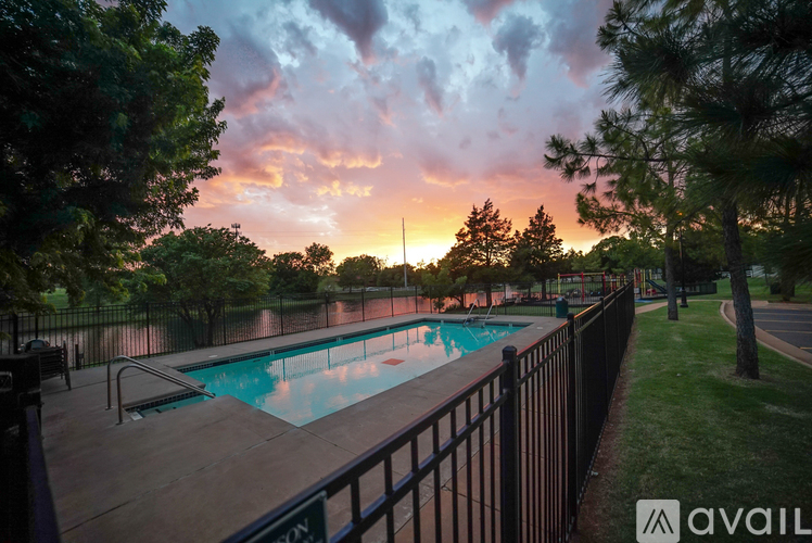 A pool surrounded by a fence with trees and a sunset in the background.