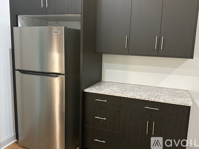 A stainless steel refrigerator stands next to a counter with cabinets above it.