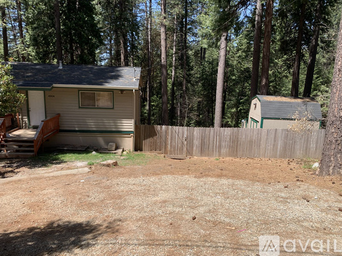 A small house with a fence and trees in the background.
