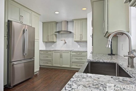 A kitchen with a stainless steel refrigerator and a marble countertop.