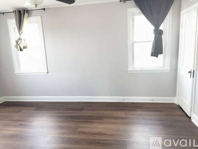 A room with a wooden floor and a window with a grey curtain.