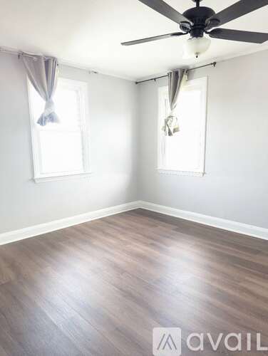 A room with a ceiling fan and two windows with curtains.
