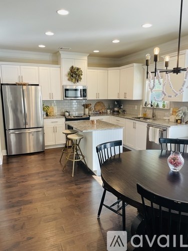 A kitchen with a table and chairs in the foreground and a refrigerator, microwave, and oven in the background.
