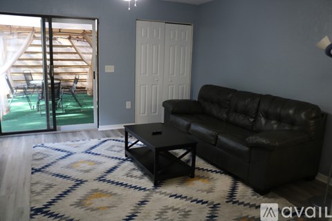 A black leather couch sits in a living room with a rug and a coffee table.