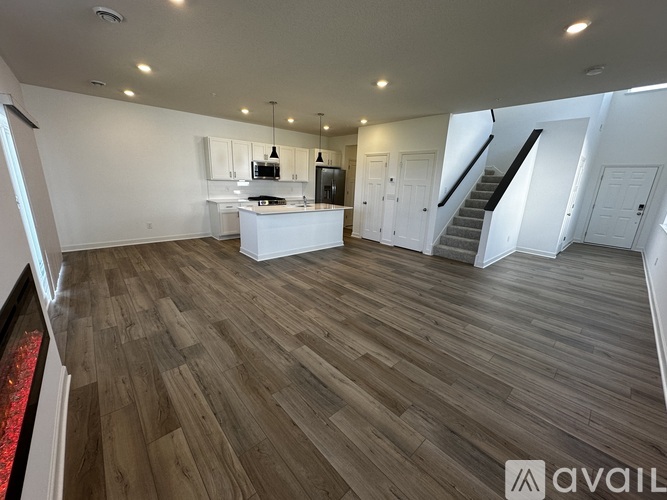 A spacious room with wooden flooring and a staircase.
