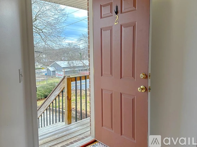 A pink door with a gold handle is open to a deck with a view of a house and trees.