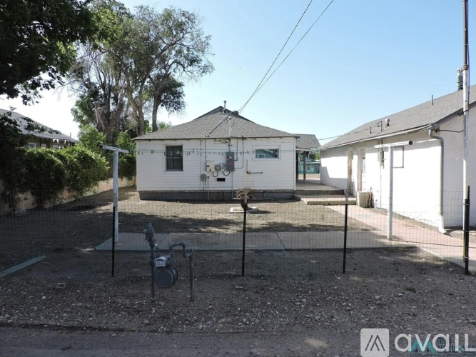 A white building with a black roof is surrounded by a fence and has a sign that reads "AVAILABLE".